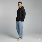 Man wearing a black hoodie and light blue jeans on a gray background