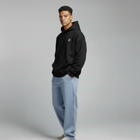 Man wearing a black hoodie and light blue jeans on a gray background
