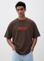 Man wearing a brown t-shirt with 'HUSTLE' in red text on a white background