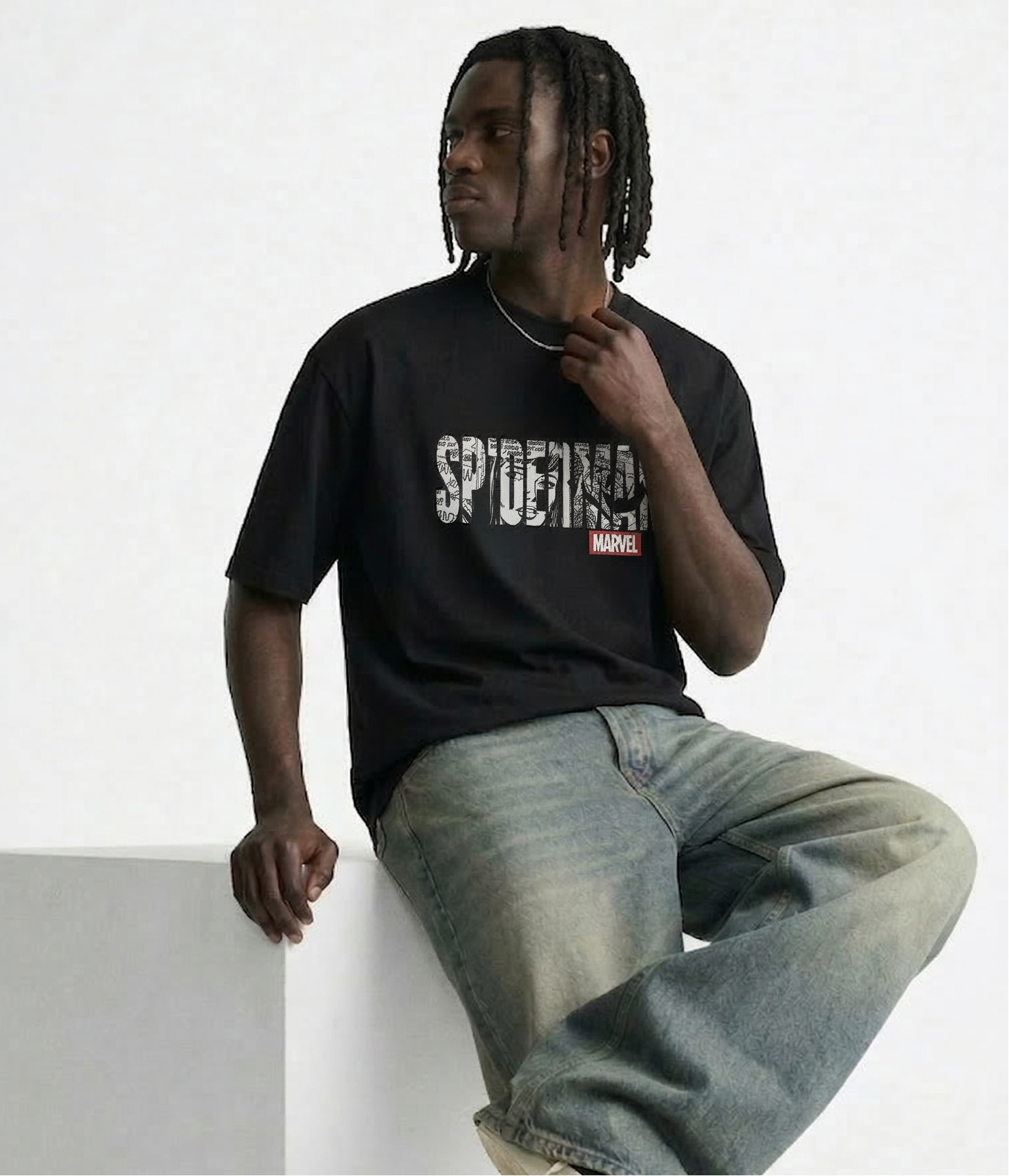 Person wearing a black t-shirt with 'Spider-Man' logo and blue jeans sitting against a white wall.