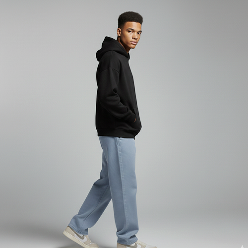 Man wearing a black hoodie and light blue jeans on a gray background
