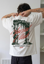 Person wearing a white t-shirt with a graphic design and text, standing indoors.