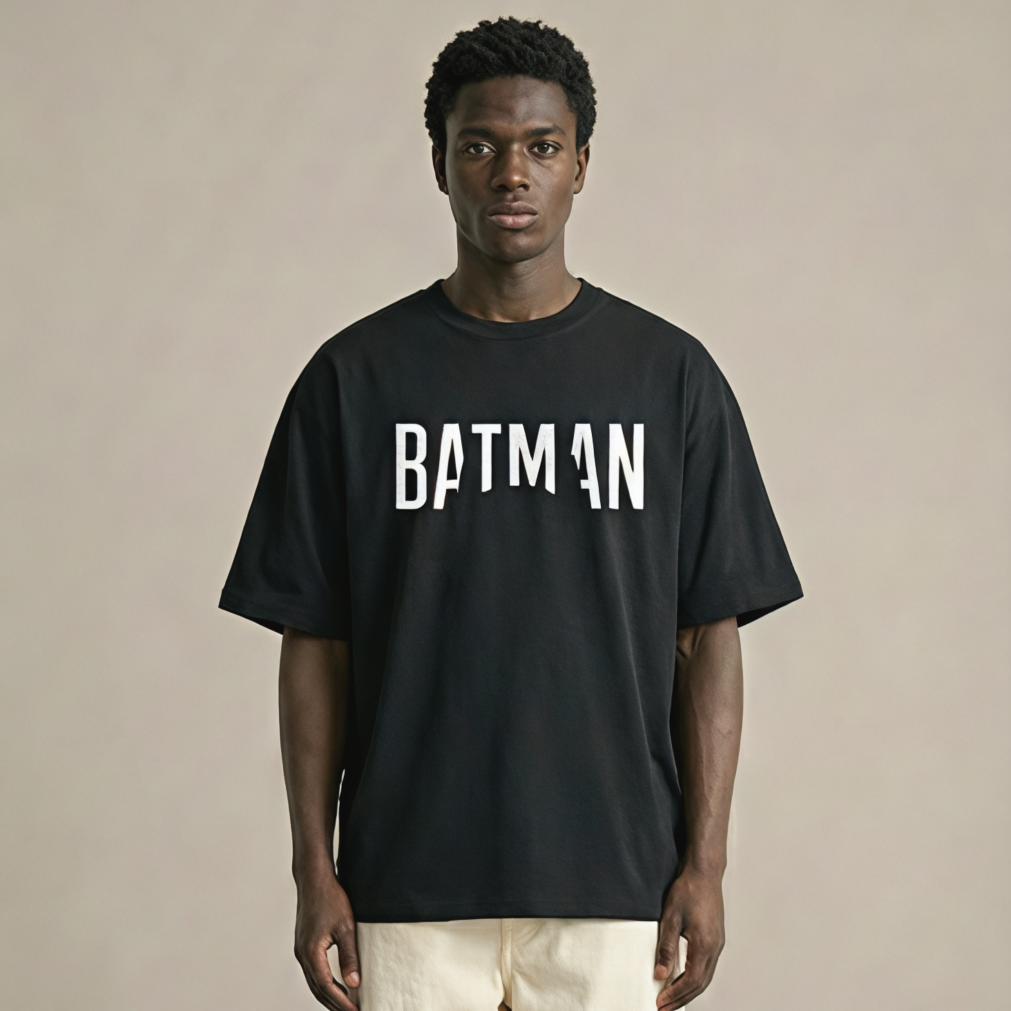 Person wearing a black 'BATMAN' t-shirt on a beige background