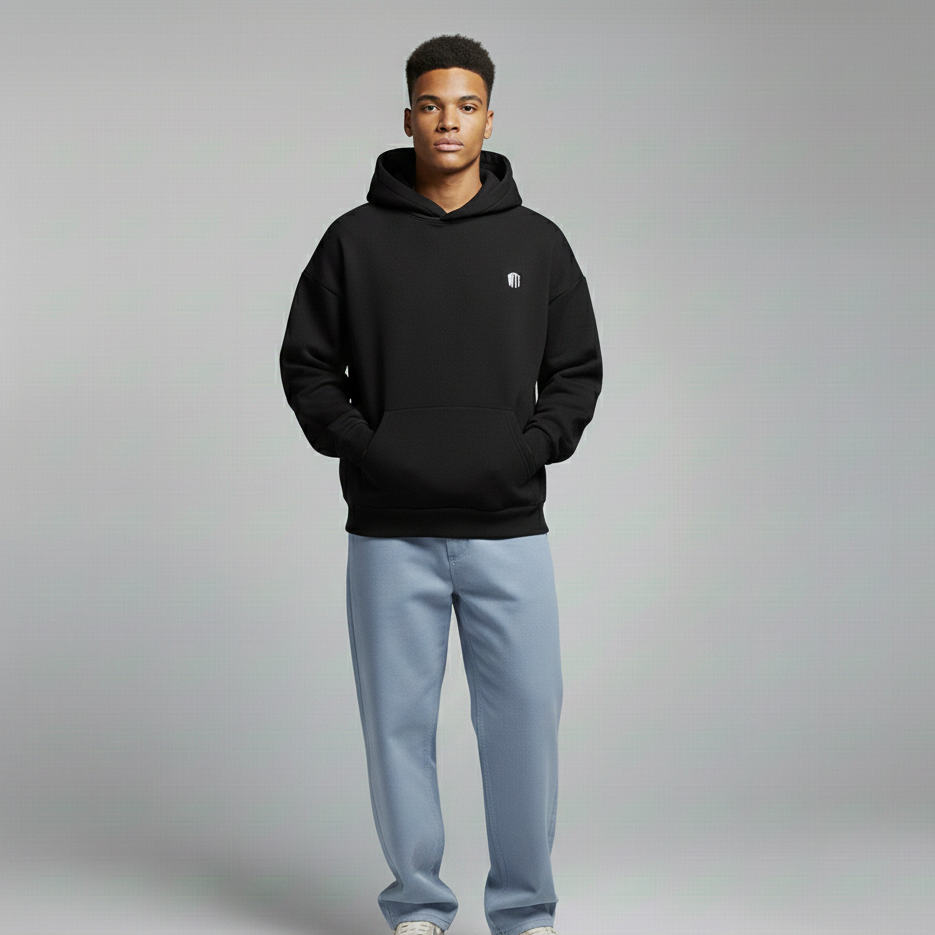 Person wearing a black hoodie with a logo, light blue jeans, and white sneakers on a gray background