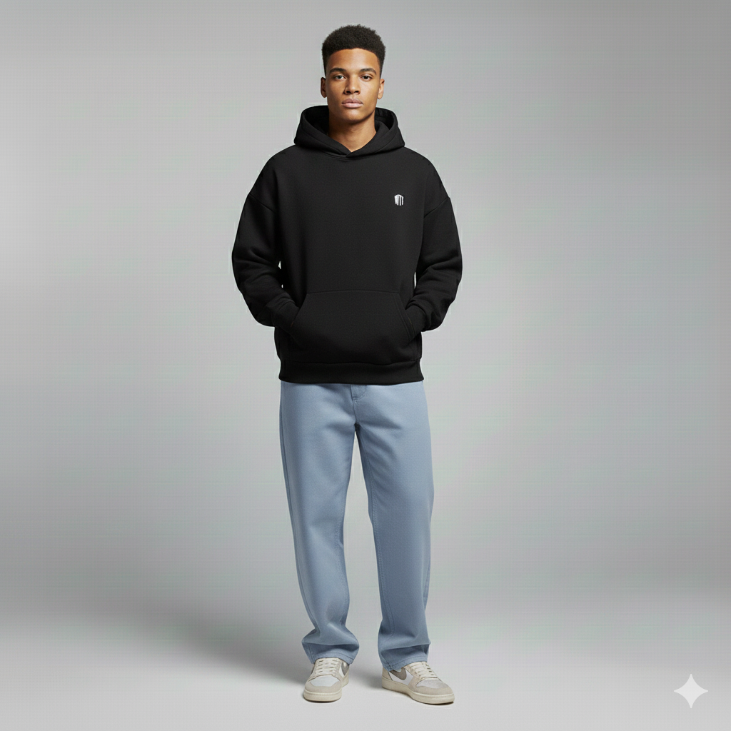 Person wearing a black hoodie with a logo, light blue jeans, and white sneakers on a gray background