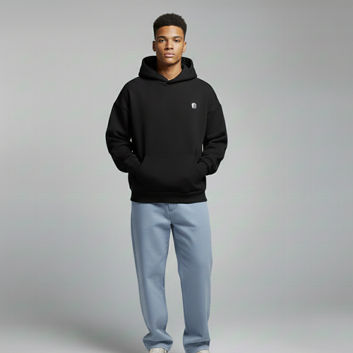 Person wearing a black hoodie with a logo, light blue jeans, and white sneakers on a gray background