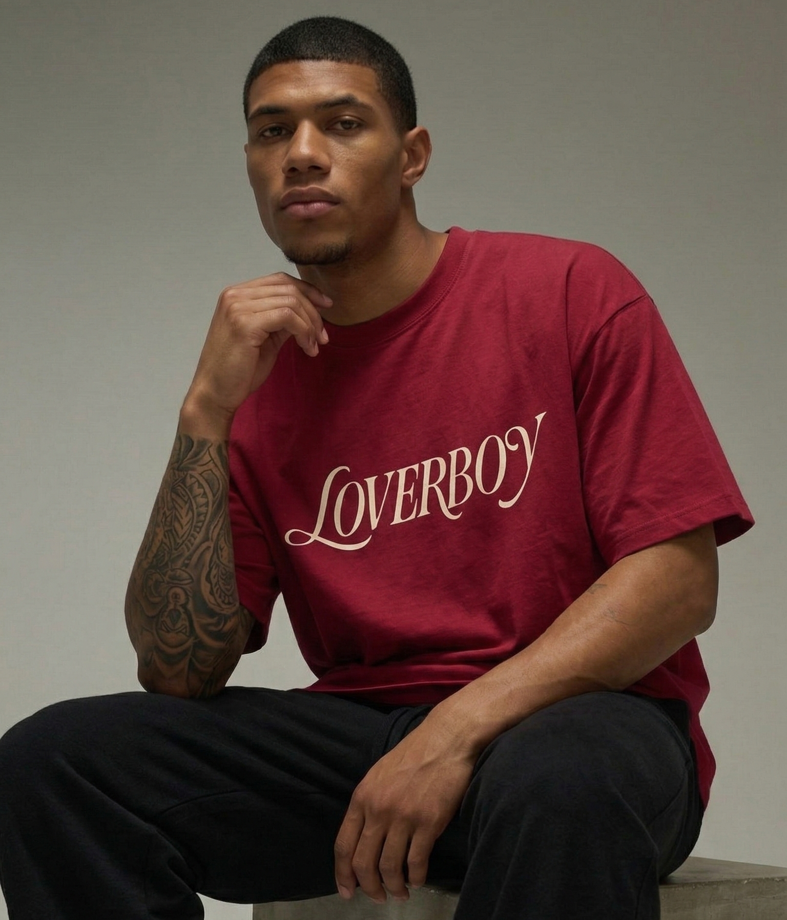 Person wearing a red 'LOVERBOY' t-shirt sitting on a concrete block.