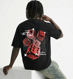 Person wearing a black t-shirt with a colorful design on the back, sitting on a white block.