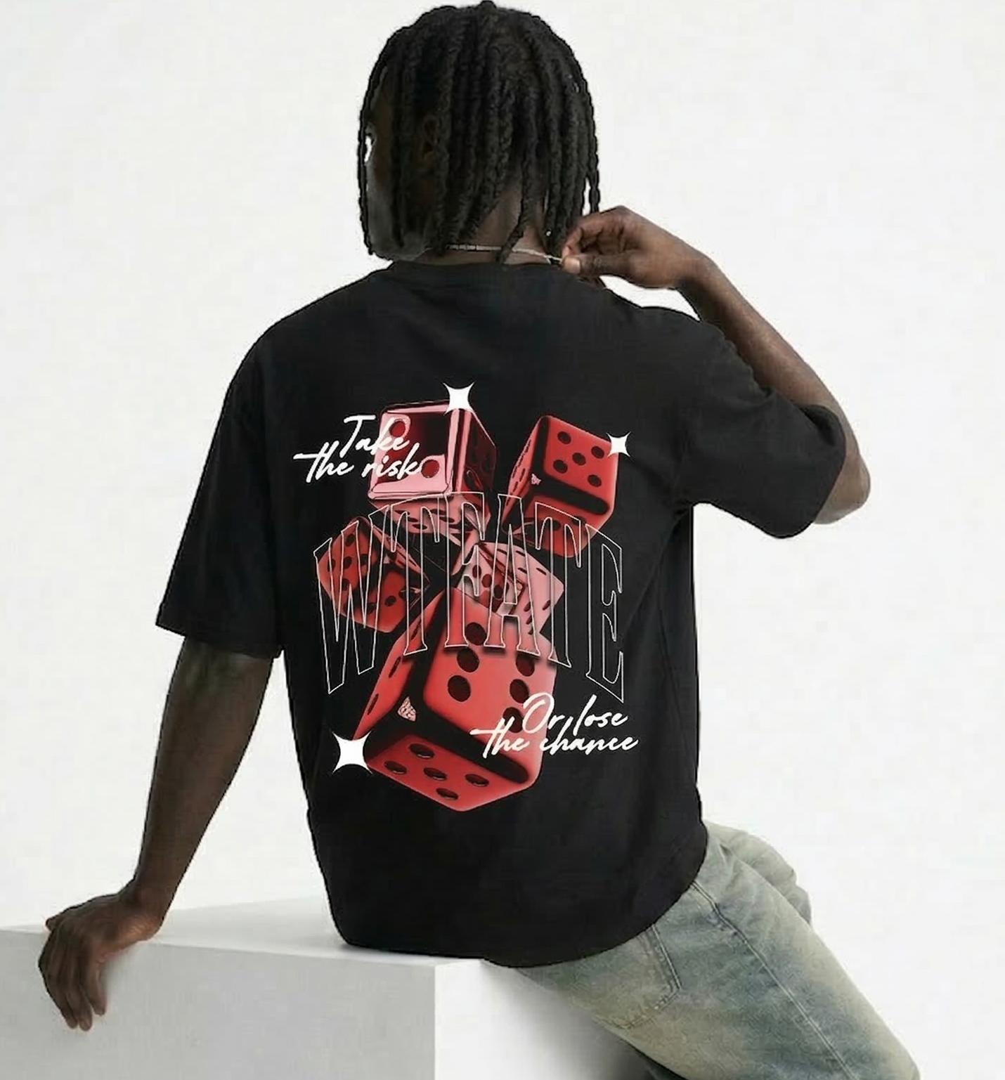 Person wearing a black t-shirt with a colorful design on the back, sitting on a white block.