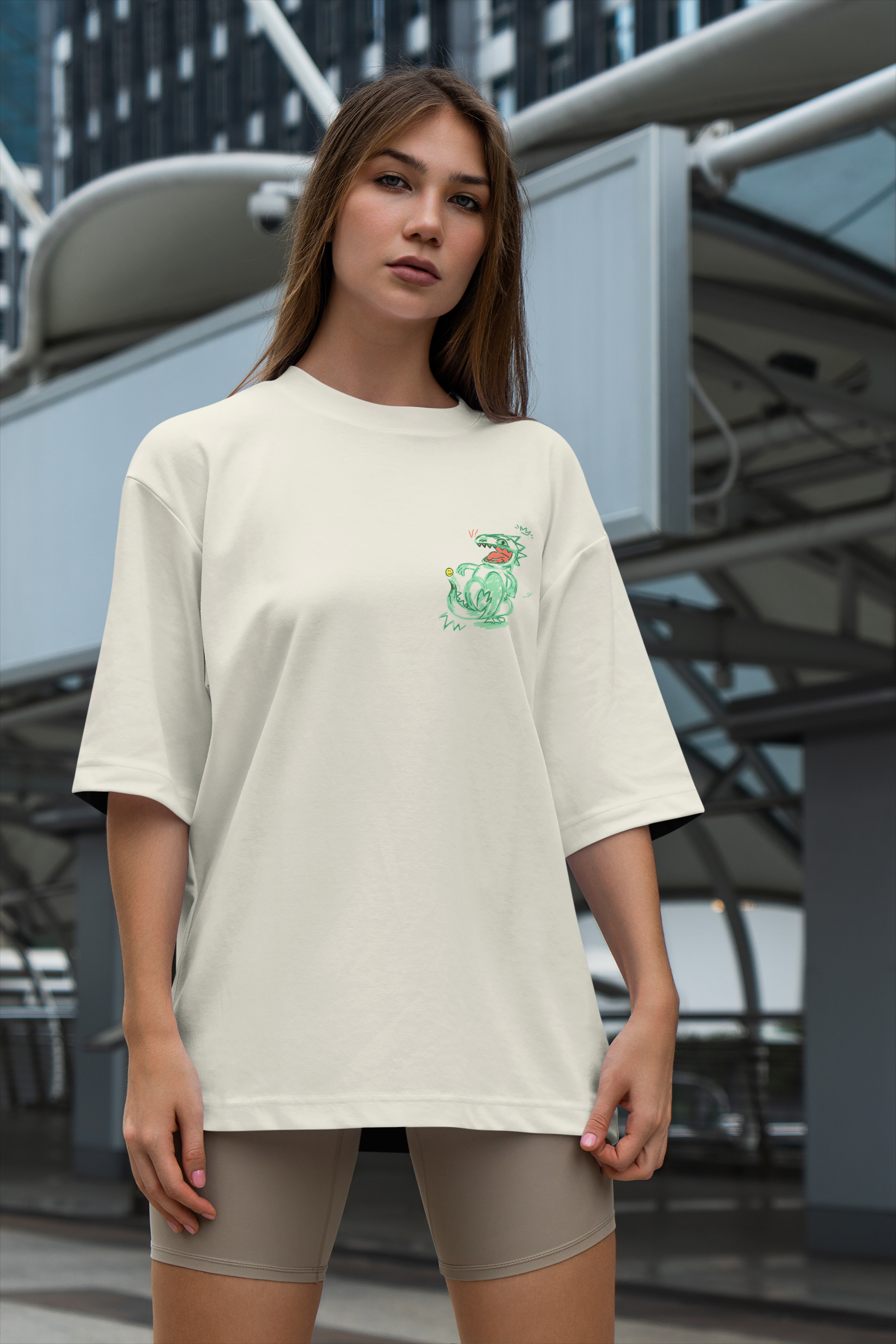 Woman wearing a beige oversized t-shirt with a small green logo in an urban setting