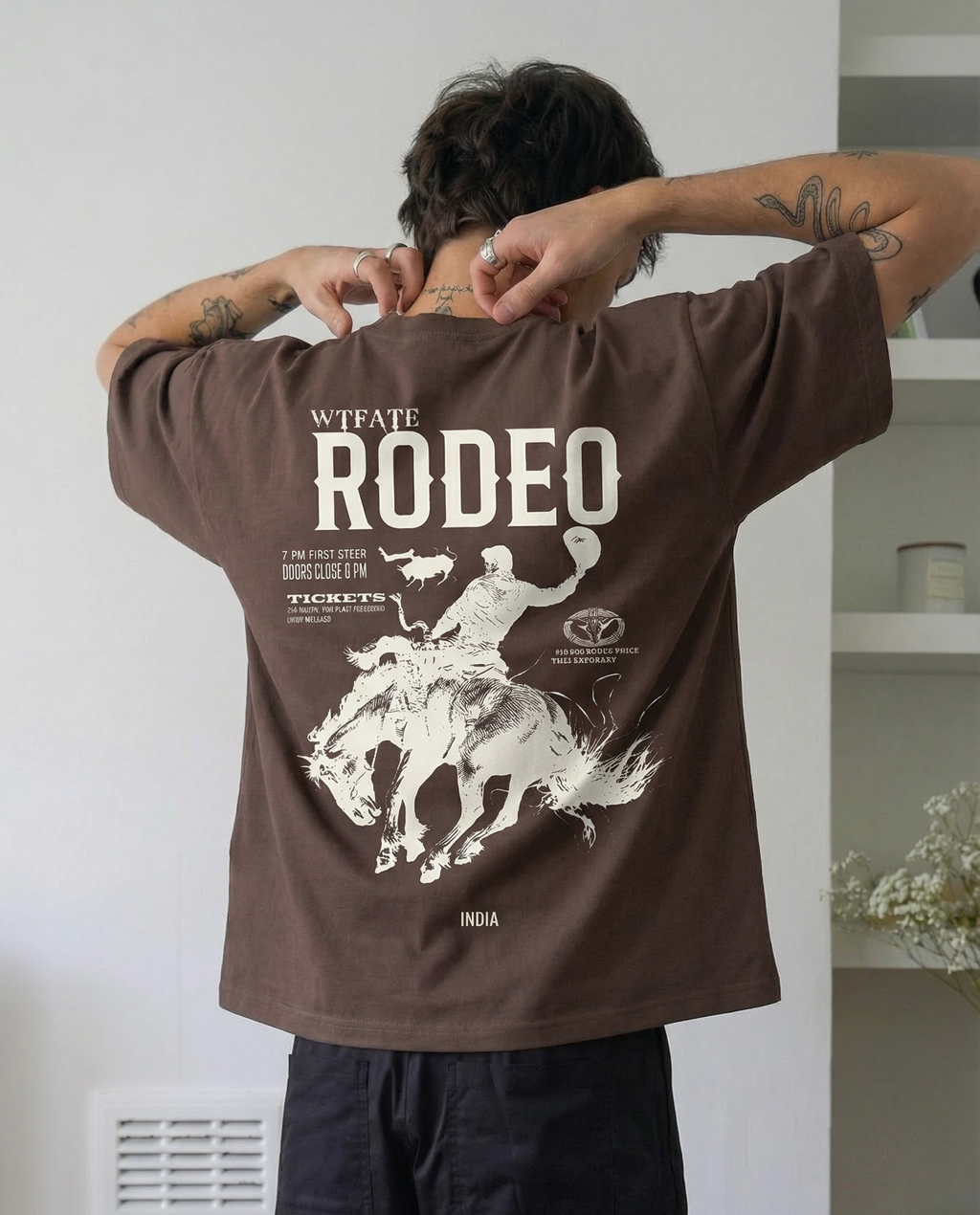 Person wearing a brown 'Rodeo' t-shirt with graphic design on the back, standing indoors.