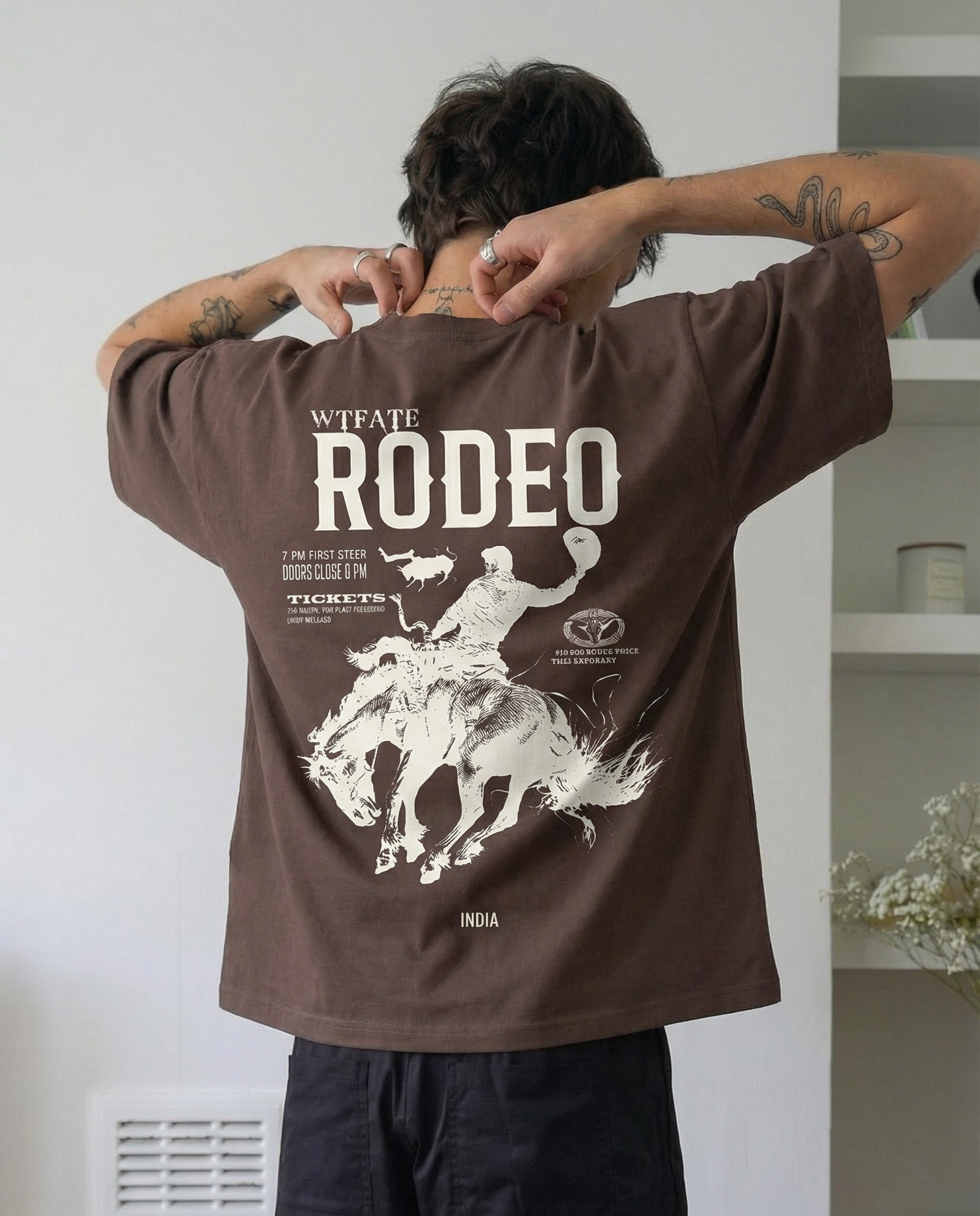 Person wearing a brown 'Rodeo' t-shirt with graphic design on the back, standing indoors.